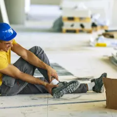 Budowlaniec w niebieskim kasku siedzi na podłodze, trzymając się za bolącą kostkę. Protokół powypadkowy sporządza się w terminie nie późniejszym niż.