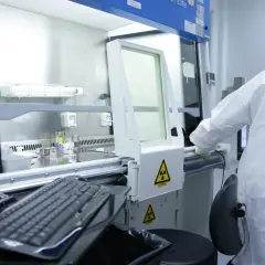 Pracownik w kombinezonie ochronnym pracuje w laboratorium, gdzie widoczne są ostrzeżenia o promieniowaniu radioaktywnym.