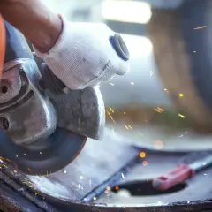 Ręka w rękawicy trzyma szlifierkę kątową, która generuje iskry i drgania mechaniczne podczas pracy.