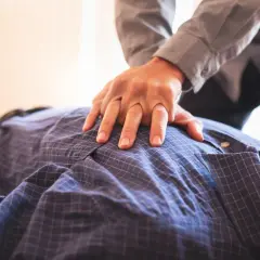 Ręce na klatce piersiowej mężczyzny, który mógł doznać **ataku serca**. Ktoś udziela pierwszej pomocy.