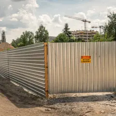 Ogrodzenie budowy z blachy falistej, z tabliczką "Uwaga wyjazd z budowy". Spełnia wymagania bezpieczeństwa.