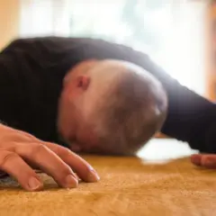 Mężczyzna leży na podłodze, jego głowa jest opuszczona, a ręce wyciągnięte. Wygląda na to, że przeżywa atak padaczki.