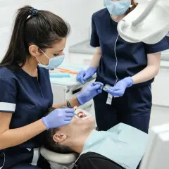 Dentystka w masce i rękawiczkach bada zęby pacjenta w gabinecie stomatologicznym.