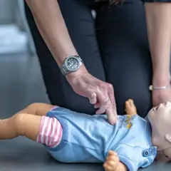 Ćwiczenie reanimacji a resuscytacji niemowlaka na fantomie. Dłoń instruktora uciska klatkę piersiową.