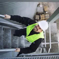 Pracownik w kamizelce odblaskowej i kasku na schodach. To przykład, jak dbałość o bhp co to znaczy w praktyce.