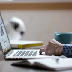Osoba pracuje na laptopie, szukając informacji o kurs na inspektora bhp cena. Na biurku leży notatnik.
