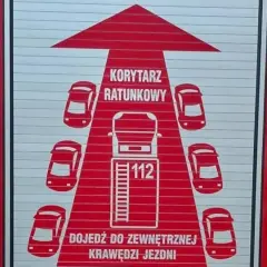 Na drzwiach wozu strażackiego widnieje grafika "KORYTARZ RATUNKOWY" z samochodami i numerem 112.