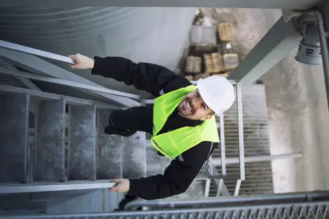 Pracownik w kamizelce odblaskowej i kasku na schodach. To przykład, jak dbałość o bhp co to znaczy w praktyce.