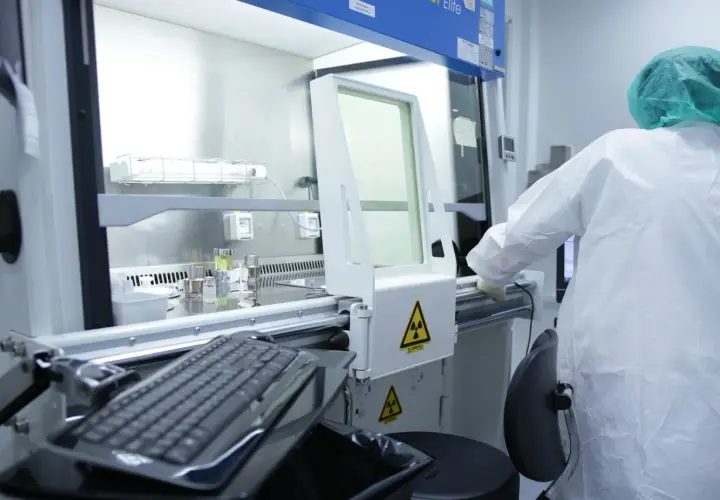 Pracownik w kombinezonie ochronnym pracuje w laboratorium, gdzie widoczne są ostrzeżenia o promieniowaniu radioaktywnym.