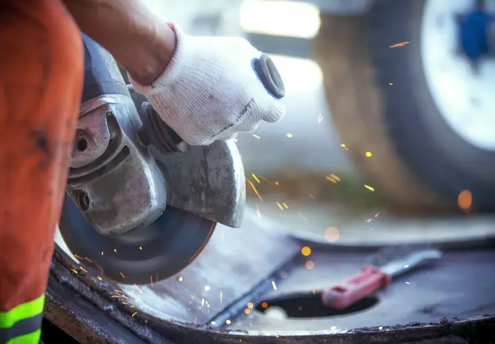 Ręka w rękawicy trzyma szlifierkę kątową, która generuje iskry i drgania mechaniczne podczas pracy.