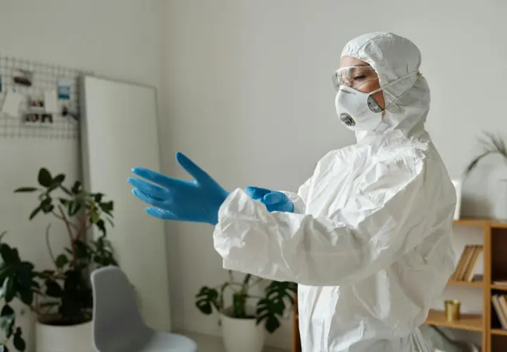 Osoba w kombinezonie ochronnym zakłada niebieskie rękawiczki, przygotowując się do pracy z czynnikami biologicznymi.