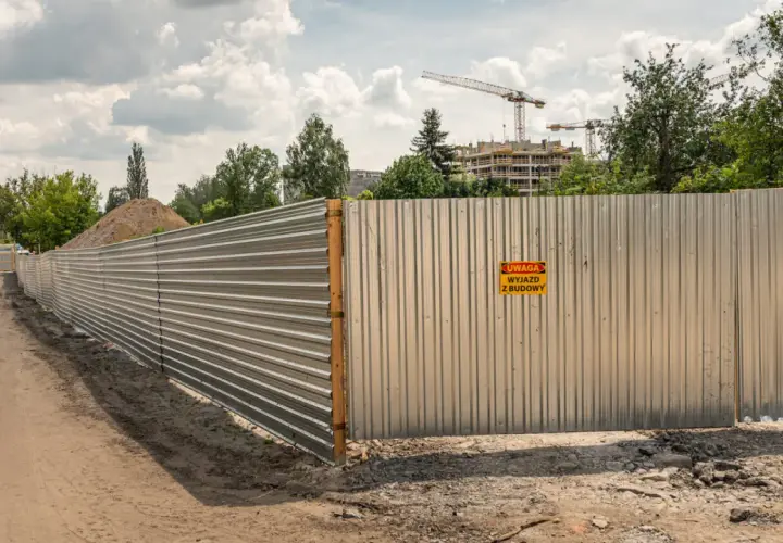 Ogrodzenie budowy z blachy falistej, z tabliczką "Uwaga wyjazd z budowy". Spełnia wymagania bezpieczeństwa.