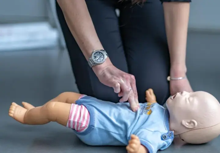 Ćwiczenie reanimacji a resuscytacji niemowlaka na fantomie. Dłoń instruktora uciska klatkę piersiową.
