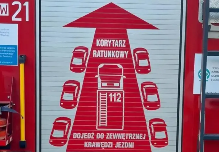 Na drzwiach wozu strażackiego widnieje grafika "KORYTARZ RATUNKOWY" z samochodami i numerem 112.