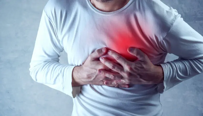 Mężczyzna trzyma się za klatkę piersiową, gdzie widoczny jest czerwony obszar bólu. Czuje ostry ból w klatce piersiowej przy oddychaniu.