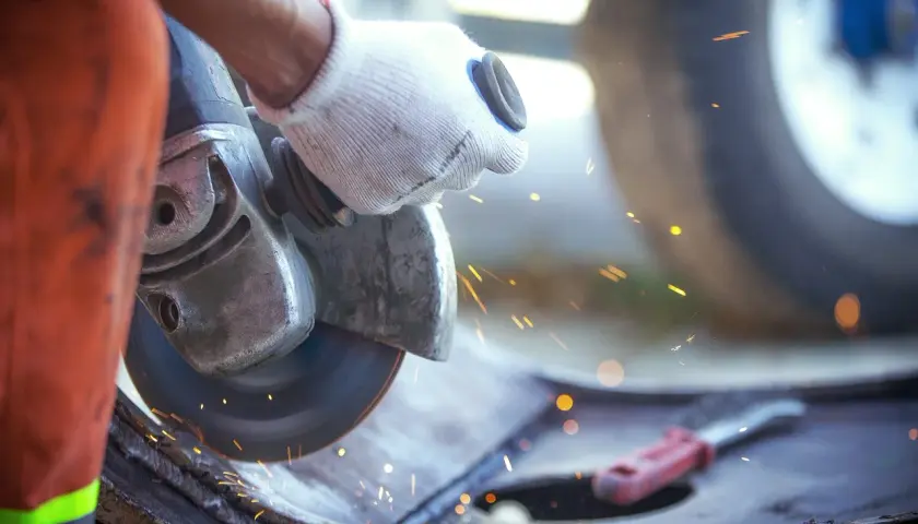 Ręka w rękawicy trzyma szlifierkę kątową, która generuje iskry i drgania mechaniczne podczas pracy.