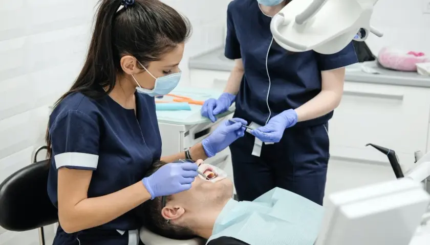 Dentystka w masce i rękawiczkach bada zęby pacjenta w gabinecie stomatologicznym.