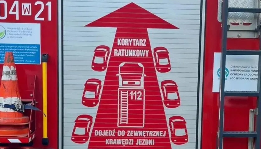 Na drzwiach wozu strażackiego widnieje grafika "KORYTARZ RATUNKOWY" z samochodami i numerem 112.