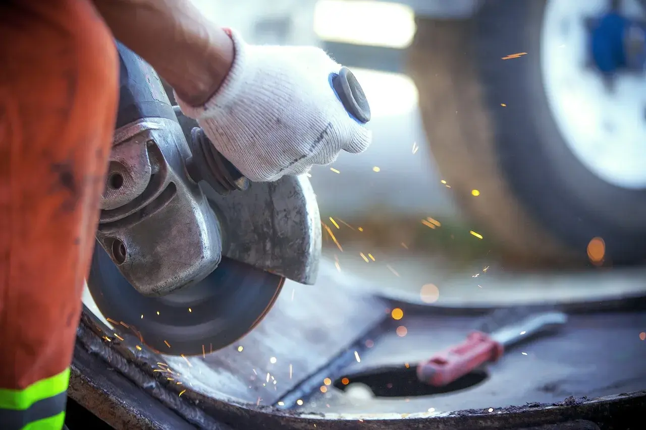 Ręka w rękawicy trzyma szlifierkę kątową, która generuje iskry i drgania mechaniczne podczas pracy.