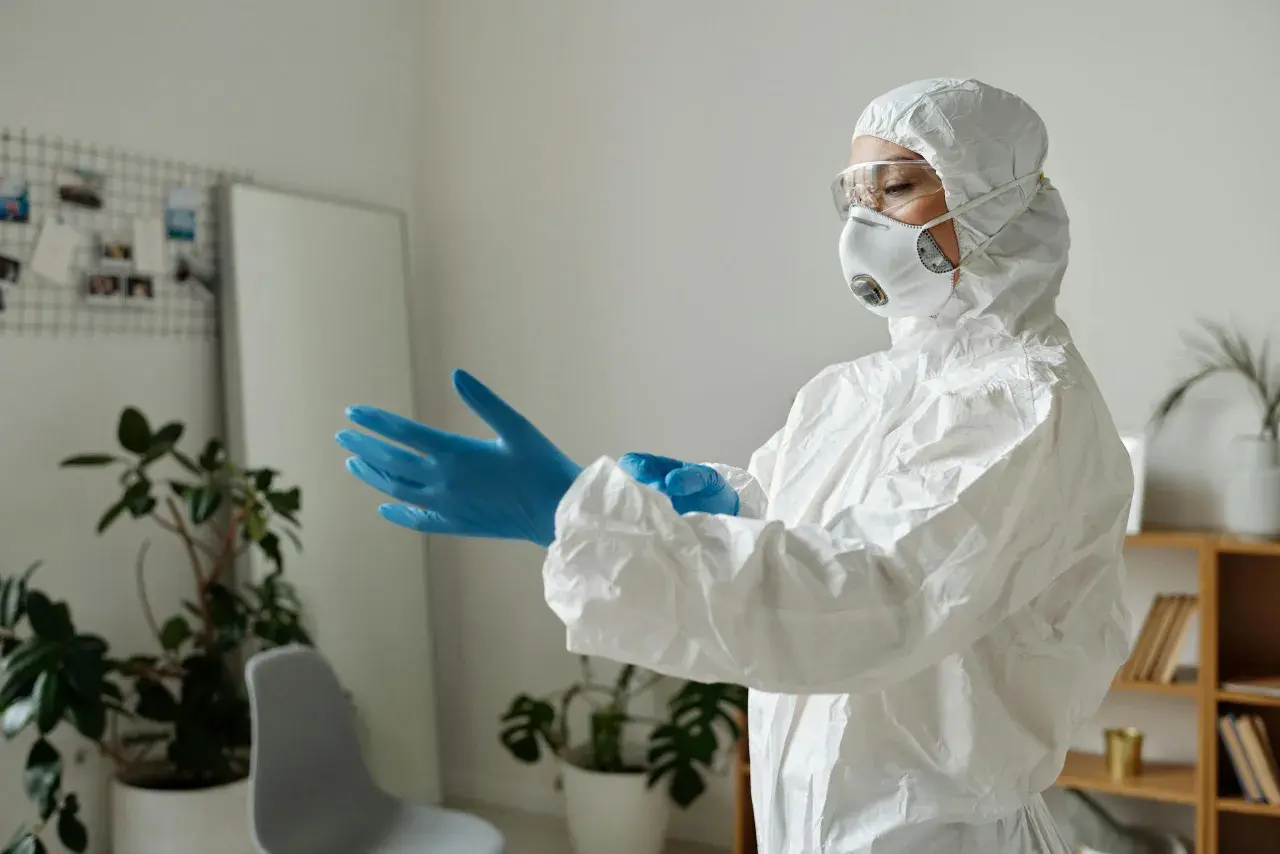 Osoba w kombinezonie ochronnym zakłada niebieskie rękawiczki, przygotowując się do pracy z czynnikami biologicznymi.